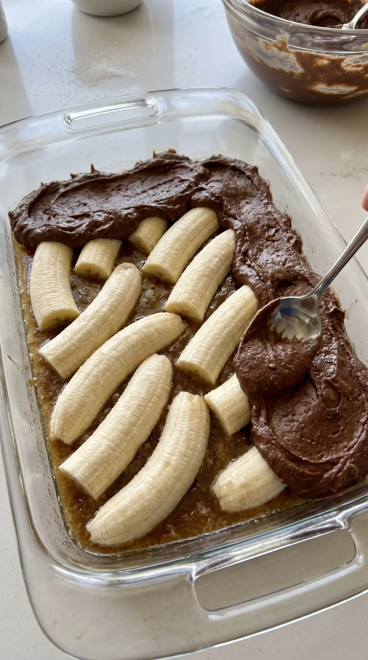 Bananas arranged in caramel layer with chocolate peanut butter batter in a baking dish