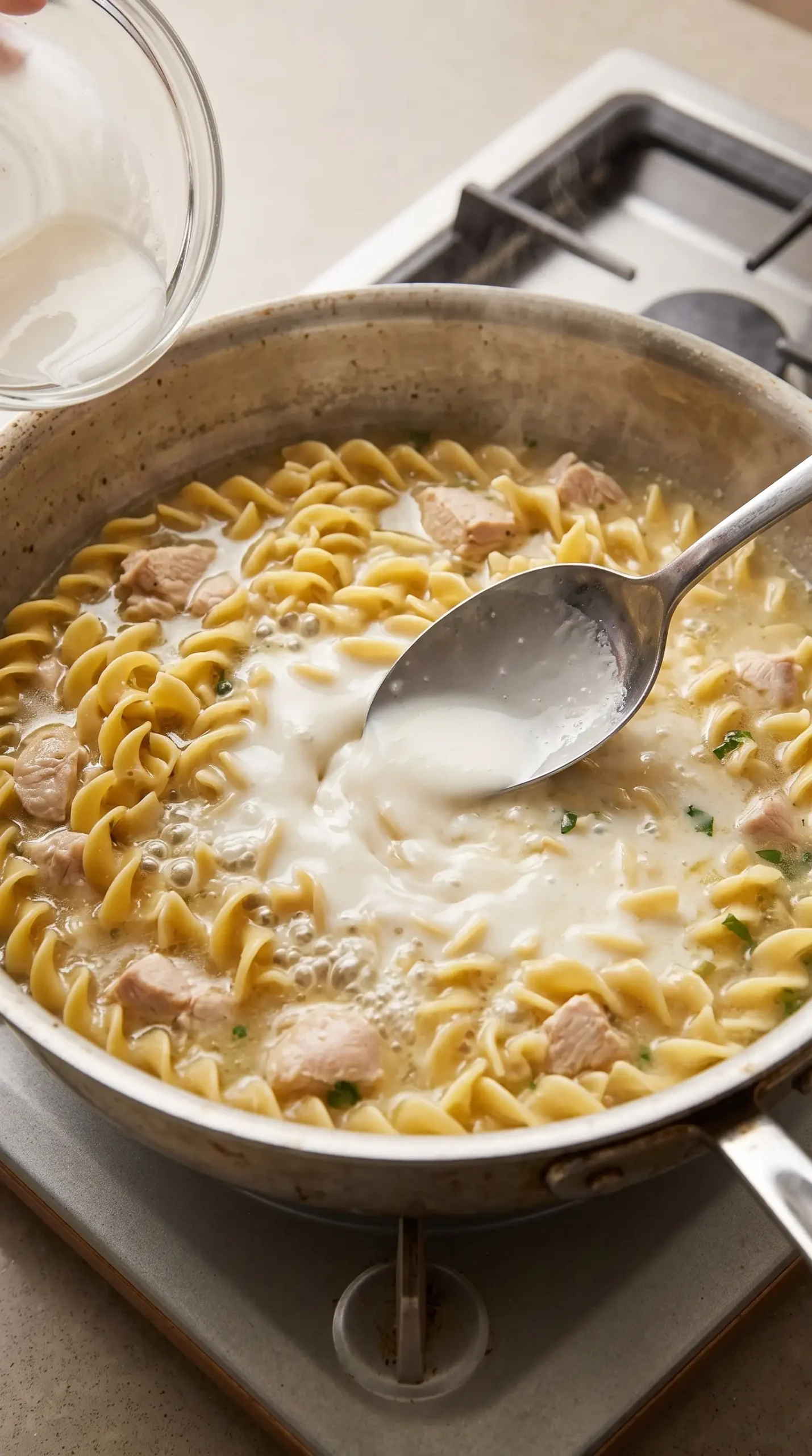 Skillet of egg noodles in chicken broth being thickened into a creamy sauce