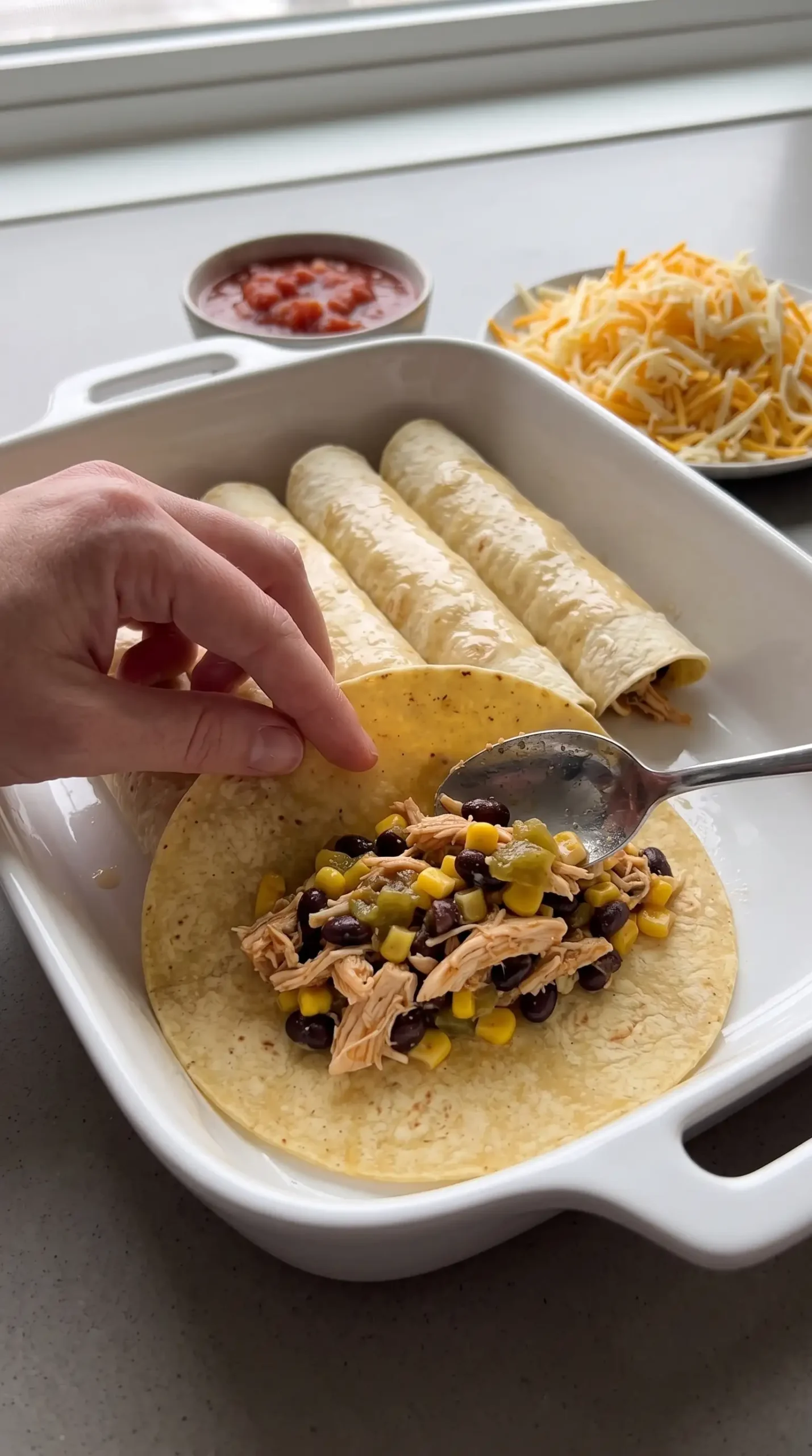 Corn tortillas filled with chicken, black beans, and corn during enchilada assembly