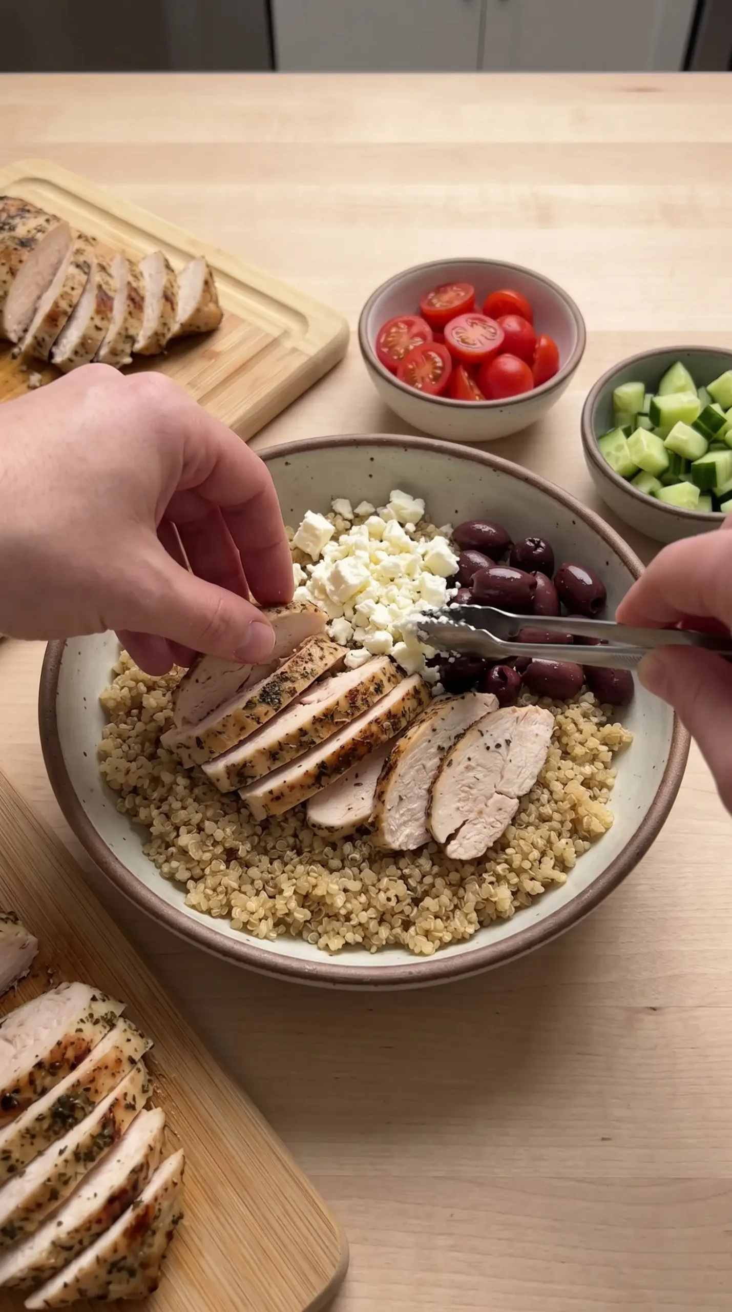 Building a Greek chicken quinoa bowl with quinoa, sliced chicken, feta, and olives