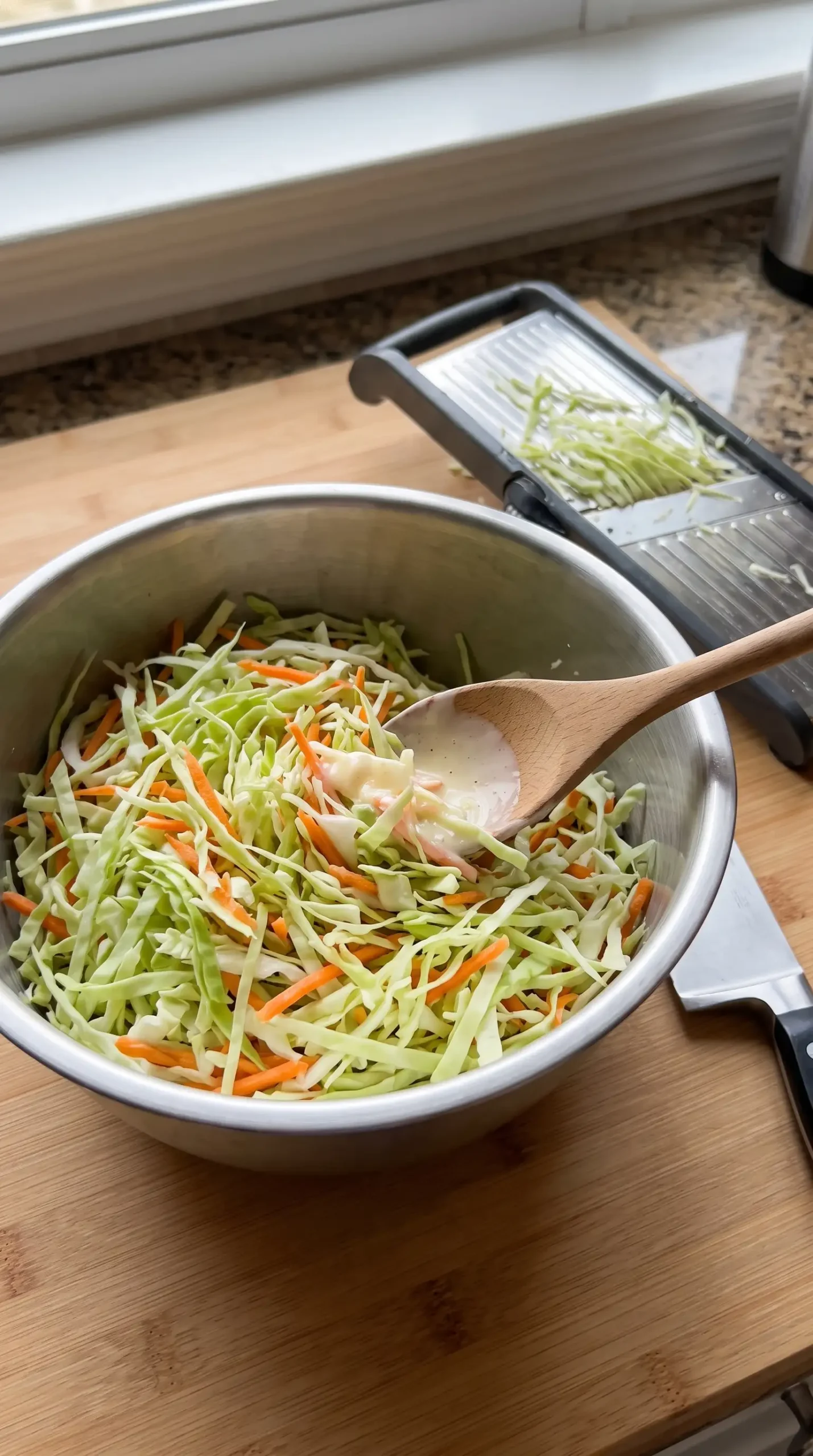 Shredded cabbage and carrots being combined while preparing creamy coleslaw