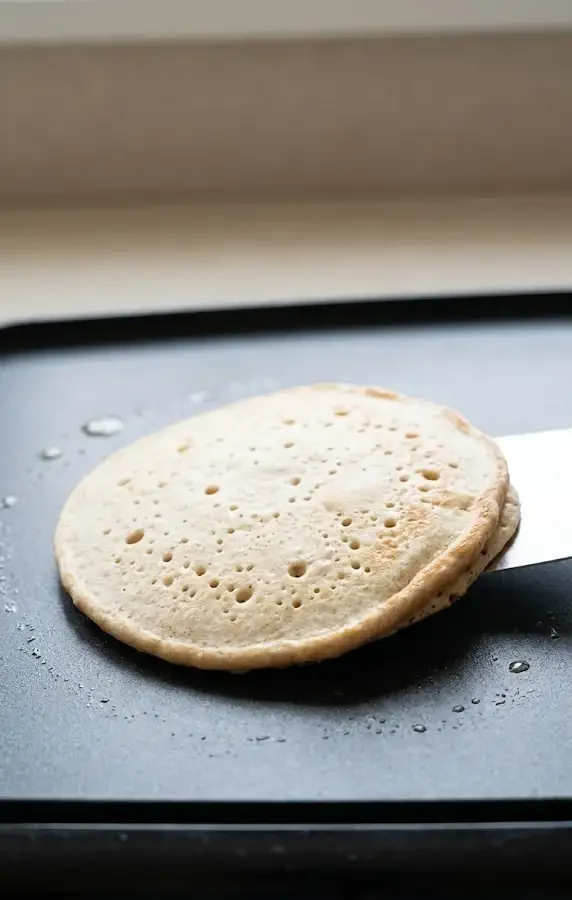 Whole wheat buttermilk pancake cooking on a griddle with bubbles forming before flipping